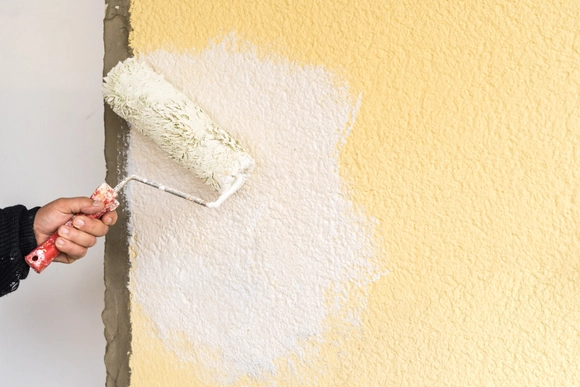 Farbrolle mit weißer Farbe wird über gelbe Wand gestrichen